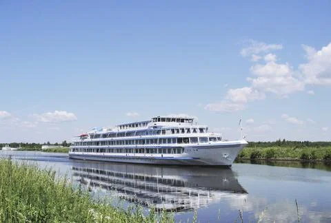 A white ship sails along the river on a clear summer day. Stock Photos