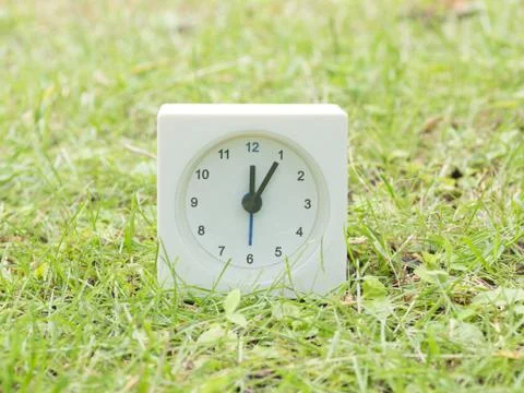 White simple clock on lawn yard, 12:05 twelve five Stock Photos