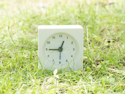 White simple clock on lawn yard, 12:45 twelve forty five Stock Photos