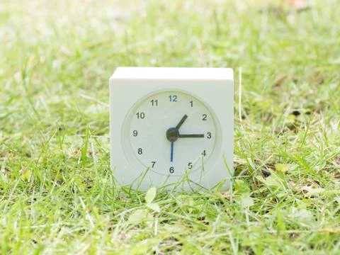 White simple clock on lawn yard, 1:15 one fifteen Stock Photos