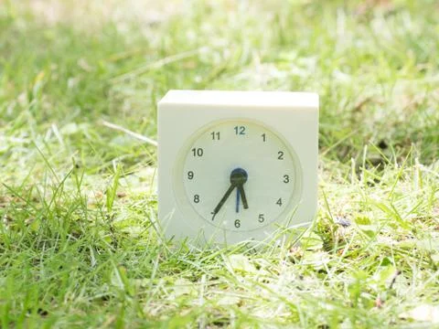 White simple clock on lawn yard, 5:35 five thirty five Stock Photos