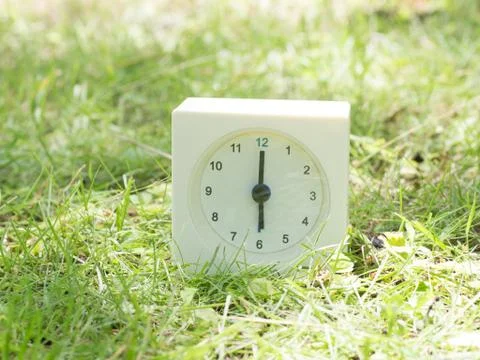 White simple clock on lawn yard, 6:00 six o'clock Stock Photos