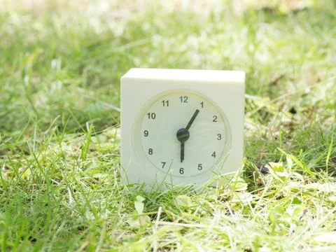 White simple clock on lawn yard, 6:05 six five Stock Photos