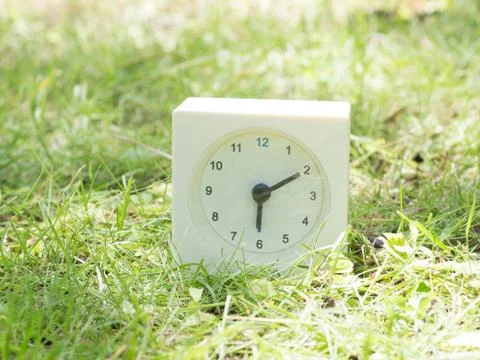 White simple clock on lawn yard, 6:10 six ten Stock Photos