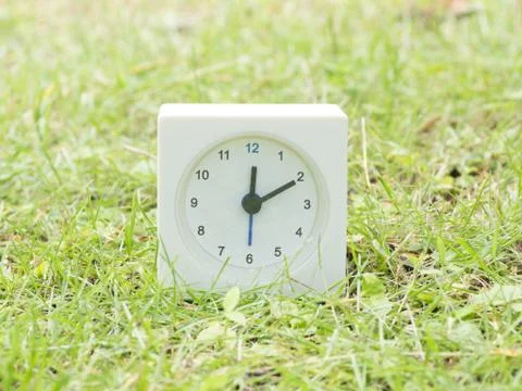 White simple clock on lawn yard, 12:10 twelve ten Stock Photos