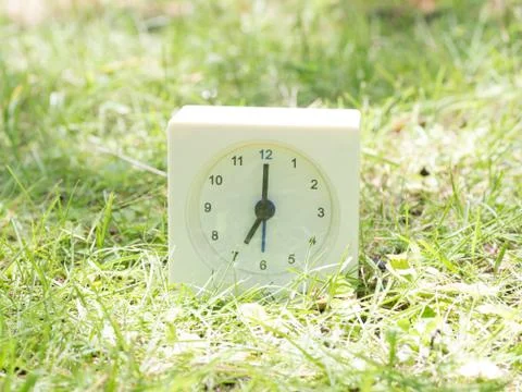 White simple clock on lawn yard, 7:00 seven o'clock Stock Photos