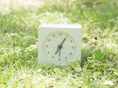 White simple clock on lawn yard, 7:05 seven five Stock Photos
