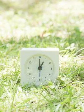 White simple clock on lawn yard, 1:00 one o'clock Stock Photos