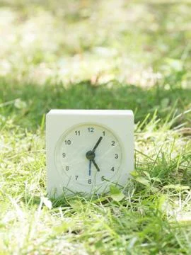 White simple clock on lawn yard, 5:05 five five Stock Photos