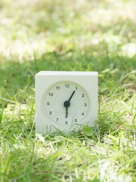 White simple clock on lawn yard, 6:05 six five Stock Photos