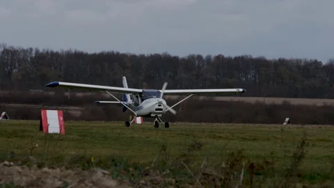 A white single-engine light plane slowly drives across the grass. Video stock 201506624