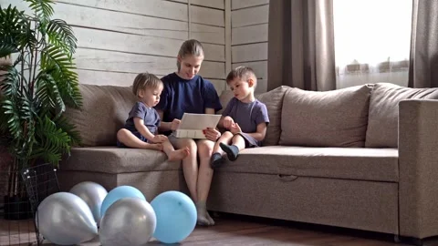 White sister reading tablet on sofa, cozy living room with wooden wall, potted Stock Footage 336975015