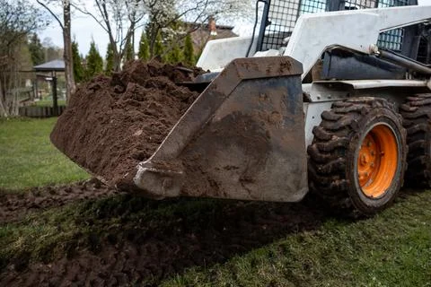 White Skid Steer Loader with Orange Wheels on Grassy Area Foto stock