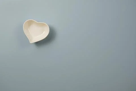 White small ceramic heart shape bowl on blue and copy space on blue background Stock Photos