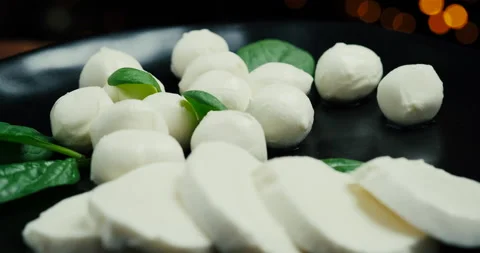 White small mozzarella cheese balls, spinach leaves on black plate. Rotaiting Stock Footage 147141271