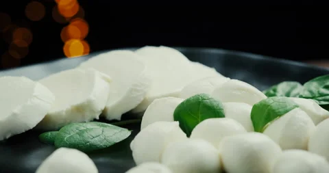 White small mozzarella cheese balls, spinach leaves on black plate. Rotaiting Stock Footage 147141527