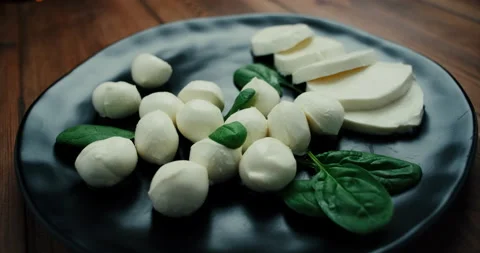 White small mozzarella cheese balls, spinach leaves on black plate. Dolly-in Stock Footage 147141860