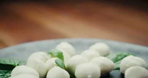 White small mozzarella cheese balls, spinach leaves and tomatoes on black plate Stock Footage 147142619