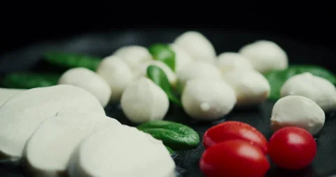White small mozzarella cheese balls, spinach leaves and tomatoes on black plate Stock Footage 147219740