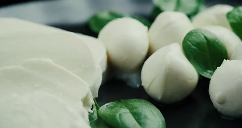 White small mozzarella cheese balls, spinach leaves on black plate. Rotaiting Stock Footage 147220029