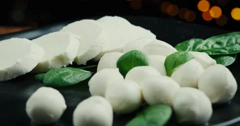 White small mozzarella cheese balls, spinach leaves on black plate. Rotaiting Stock Footage 147220330