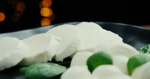 White small mozzarella cheese balls, spinach leaves on black plate. Rotaiting Stock Footage 147447654