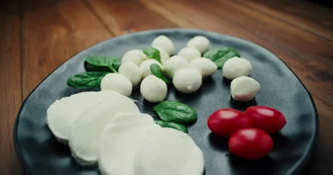 White small mozzarella cheese balls, spinach leaves and tomatoes on black plate Stock Footage 147447887