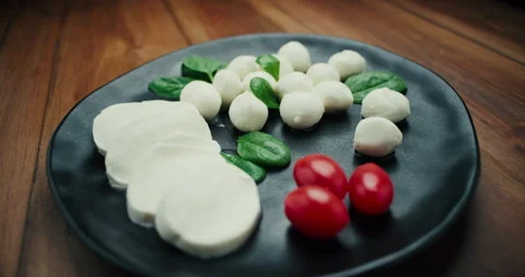 White small mozzarella cheese balls, spinach leaves and tomatoes on black plate Stock Footage 147560497