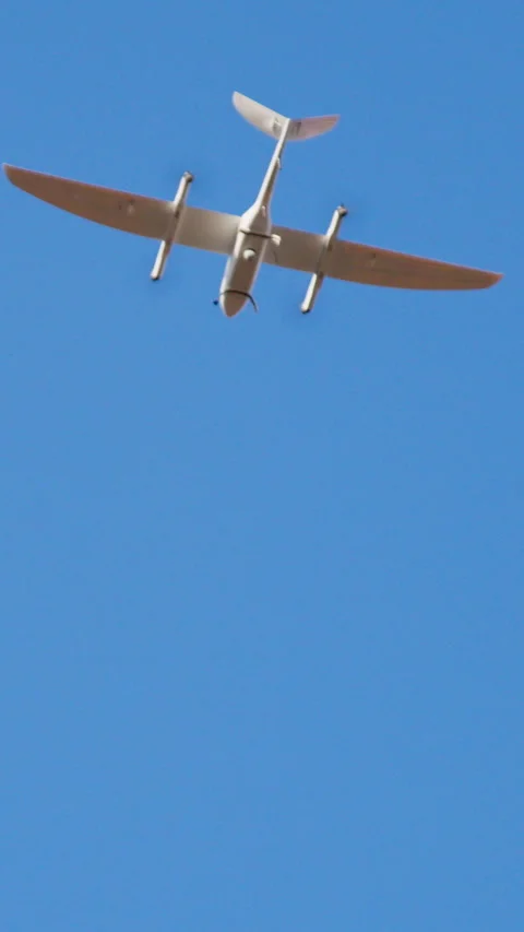 White smart drone in the shape of an airplane flies and films in the clear blue Stock Footage 314307315
