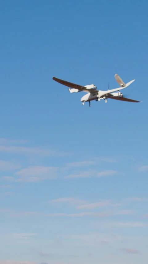 White smart drone in the shape of an airplane flies and films in the clear blue Stock Footage 314307986