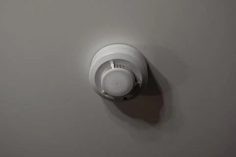 White smoke detector on white ceiling in room Stock Photos