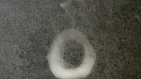 White smoke ring floating over a dark grey surface, showcasing dense 스톡 동영상 347181764
