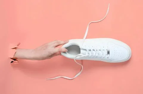 White sneaker shoe with hand pulling laces on pink background Stock Photos