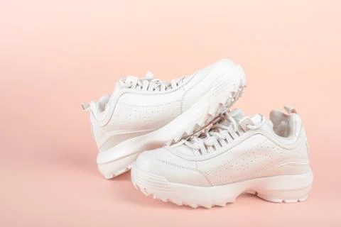 White sneakers on light pink background. Women's shoes. stylish white sneaker Stock Photos