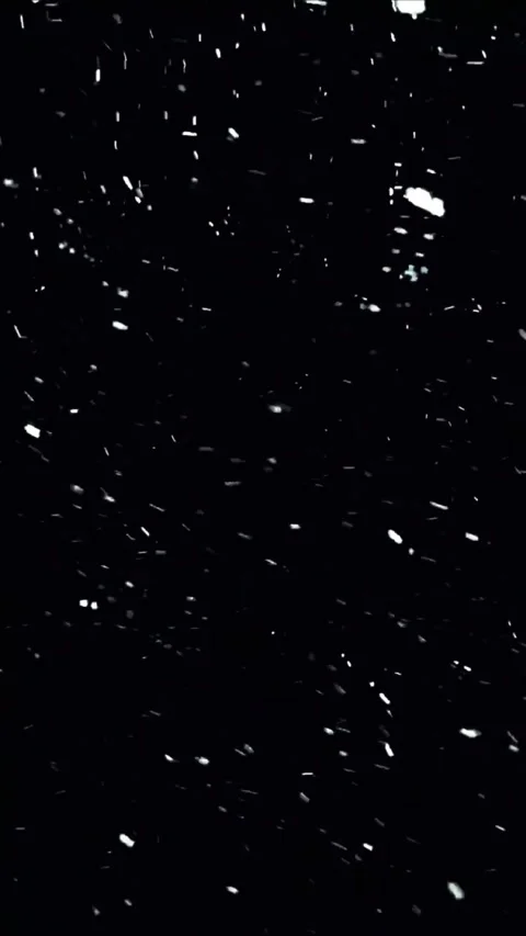 White snow particles falling against a dark black background for winter holiday Video stock 347692489