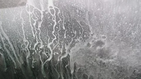 White soap foam sliding down a vehicle's windshield during an automatic car wash Stock Footage 340230720