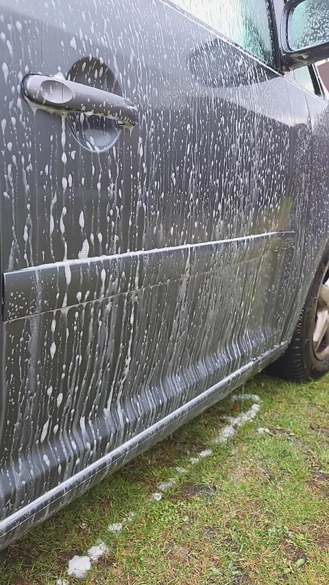 White soapy foam dripping down the side of a grey car body parked on green .. Vídeos de archivo 331959740