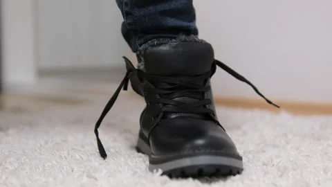 In white socks puts on black shoes pushes foot into boot on carpet tries on Stock Footage 302672907