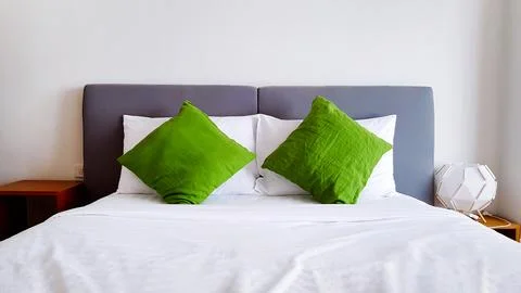 White soft bed and two green pillows with wall background. Interior design Stock Photos