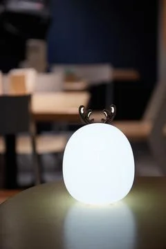 A white soft table lamp in the shape of a deer stands on a wooden table and Stock Photos