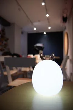 A white soft table lamp in the shape of a deer stands on a wooden table and Stock Photos