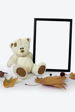 White soft toy bear with vertical frame mockup and autumn leaves with copy space Stock Photos