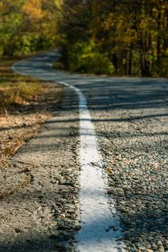 A white solid line of markings on a winding country road. In the background a Stockfoto's