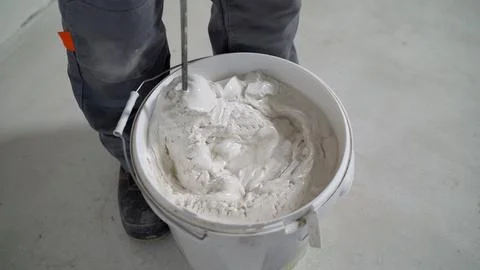 White solution in a bucket, mixed with a mixer. A worker mixes plaster in a b Stock Photos