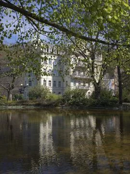 A white spa building reflected in the Tepla river framed by overhanging branches Stock Photos