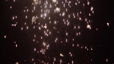 White sparks rain down in front of a dark background and later become blurred Stock Footage 80991562
