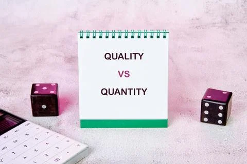 White spiral notepad features QUALITY VS QUANTITY text. Dark dice and a calcu Stock Photos