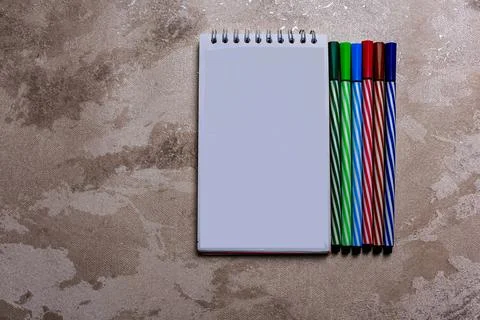 White spiral notepad placed next to five colorful striped markers on a textured Stock Photos