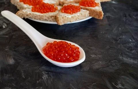White spoon with red caviar and sandwiches on dark gray  background Stock Photos