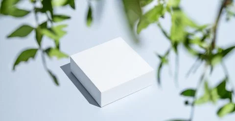 White square boxes on a blue background with shadows and green leaves. Stock Photos